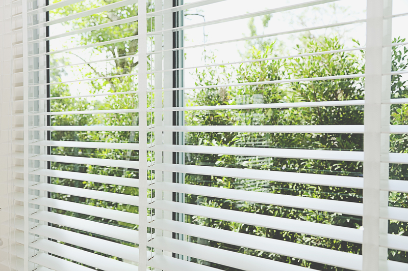 Venetian blinds with sun and greenery in background