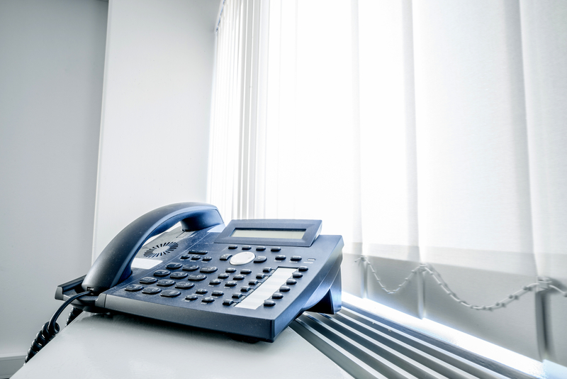 Office phone sitting next to some office blinds